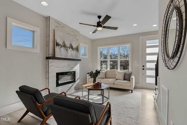 living room with ceiling fan, light hardwood / wood-style flooring, and a high end fireplace