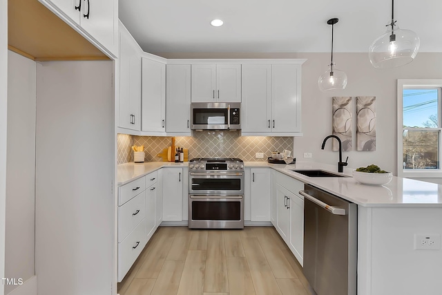 kitchen with sink, light wood-type flooring, decorative light fixtures, white cabinetry, and stainless steel appliances