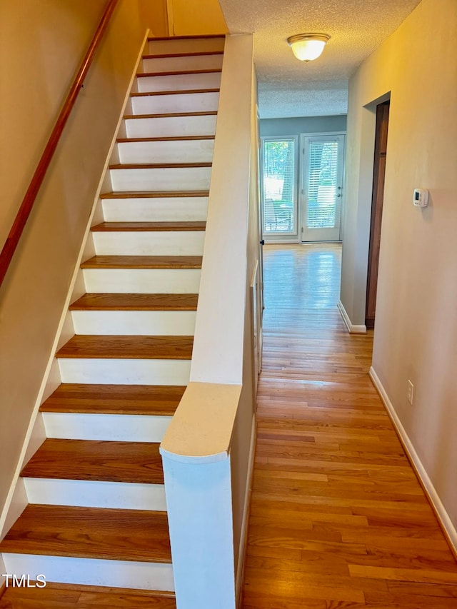 stairs with a textured ceiling and hardwood / wood-style floors