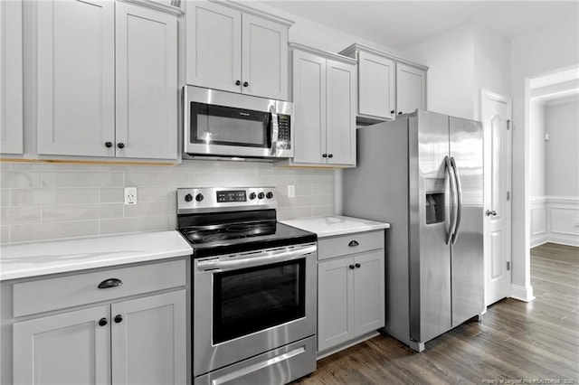 kitchen with gray cabinetry, appliances with stainless steel finishes, dark hardwood / wood-style flooring, light stone countertops, and backsplash