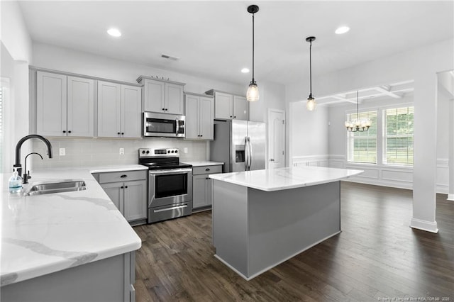 kitchen featuring sink, hanging light fixtures, a center island, light stone counters, and stainless steel appliances