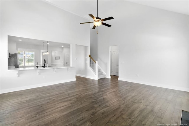 unfurnished living room featuring sink, a towering ceiling, dark wood-type flooring, and ceiling fan