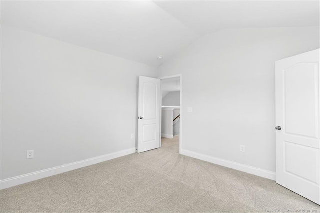 unfurnished bedroom with a spacious closet, vaulted ceiling, and light carpet