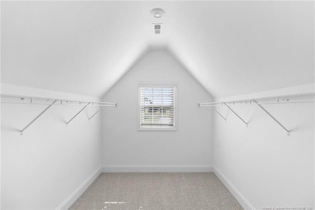 walk in closet with vaulted ceiling and light colored carpet