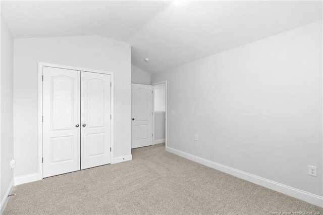 unfurnished bedroom with a closet, lofted ceiling, and light carpet