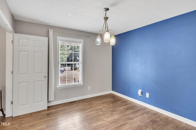 empty room featuring a textured ceiling, hardwood / wood-style floors, and a notable chandelier