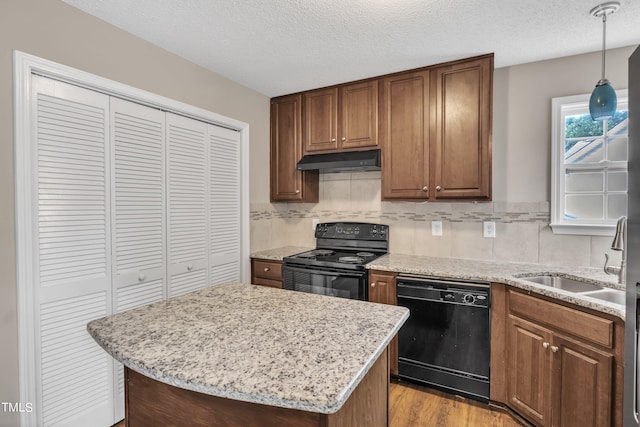 kitchen with a center island, decorative light fixtures, light wood-type flooring, black appliances, and a textured ceiling