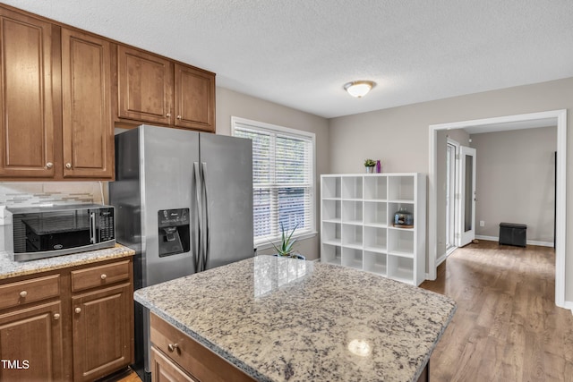 kitchen featuring a textured ceiling, stainless steel appliances, a kitchen island, light stone countertops, and hardwood / wood-style flooring