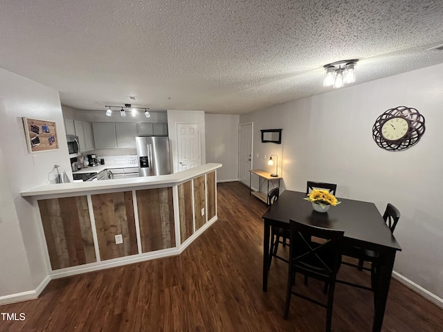 kitchen with dark wood-type flooring, kitchen peninsula, appliances with stainless steel finishes, and a textured ceiling