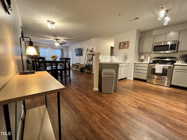 kitchen featuring stainless steel appliances, ceiling fan, a textured ceiling, dark wood-type flooring, and gray cabinets