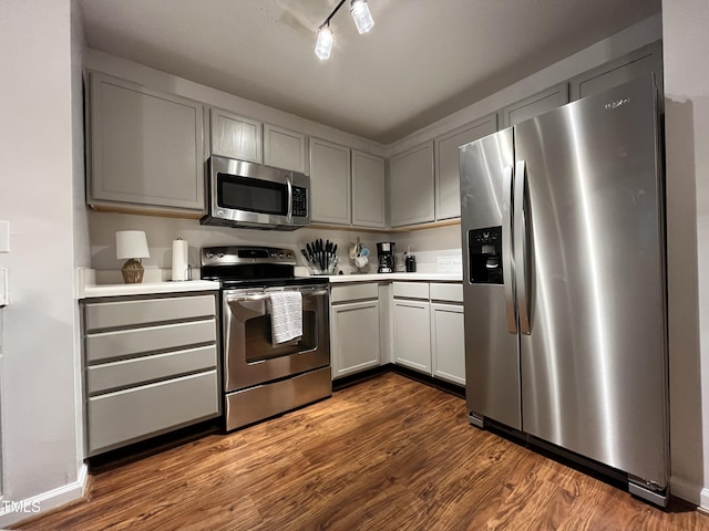 kitchen featuring track lighting, appliances with stainless steel finishes, gray cabinetry, and dark hardwood / wood-style flooring