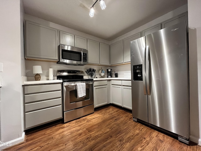 kitchen featuring dark wood-style floors, baseboards, gray cabinetry, stainless steel appliances, and light countertops