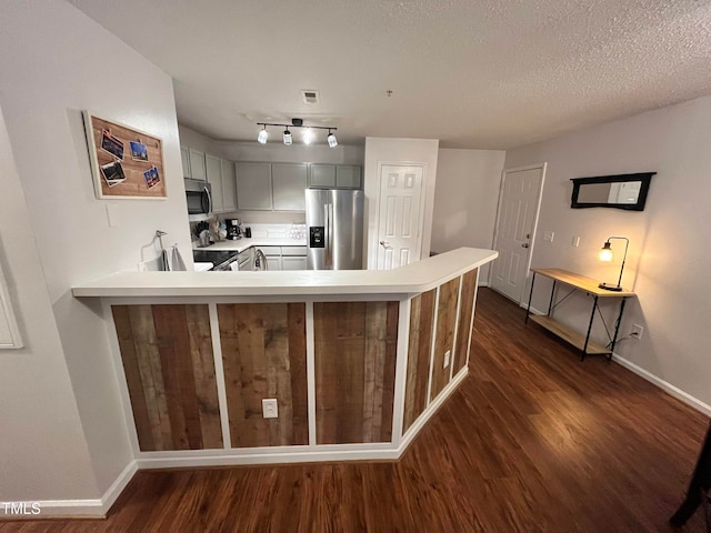 kitchen with stainless steel appliances, kitchen peninsula, a breakfast bar area, a textured ceiling, and dark wood-type flooring