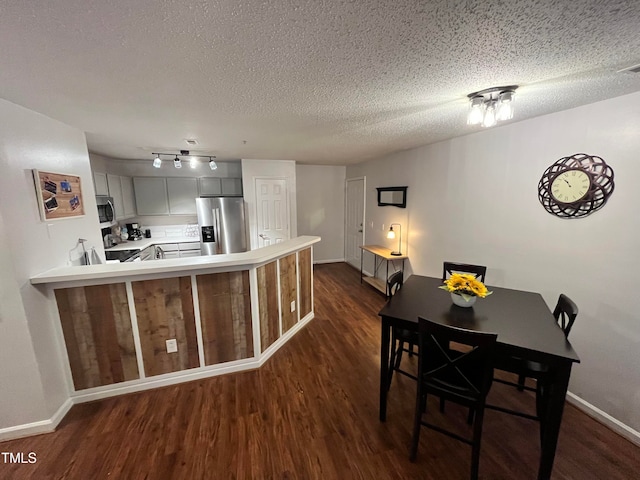 kitchen with kitchen peninsula, appliances with stainless steel finishes, a textured ceiling, and dark hardwood / wood-style flooring