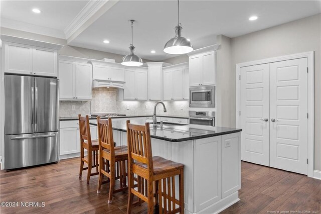 kitchen featuring dark hardwood / wood-style flooring, appliances with stainless steel finishes, a kitchen island with sink, sink, and white cabinets