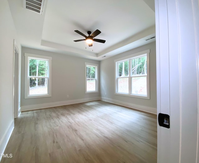 spare room featuring light wood-type flooring, a wealth of natural light, a tray ceiling, and ceiling fan