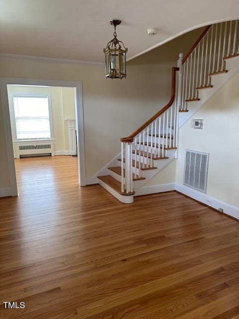 stairs with ornamental molding, radiator, hardwood / wood-style floors, and a chandelier