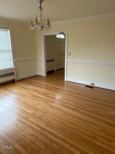 empty room featuring hardwood / wood-style floors, an inviting chandelier, and radiator heating unit