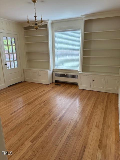 interior space featuring light wood-type flooring, ornamental molding, built in features, an inviting chandelier, and radiator