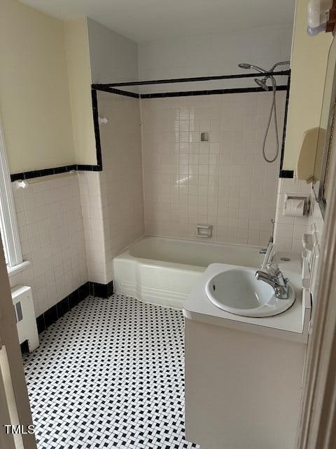 bathroom featuring tile patterned floors, tile walls, tiled shower / bath combo, radiator, and vanity