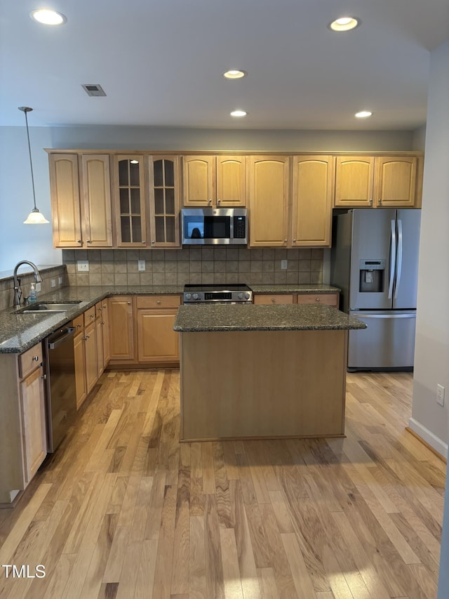 kitchen featuring sink, hanging light fixtures, light hardwood / wood-style flooring, dark stone countertops, and stainless steel appliances