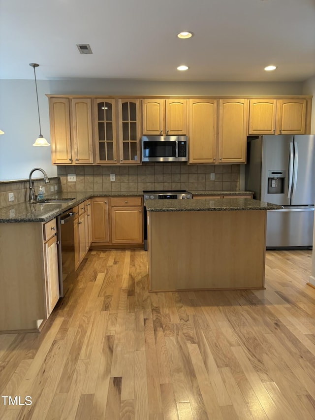 kitchen featuring light wood-type flooring, dark stone counters, stainless steel appliances, sink, and pendant lighting