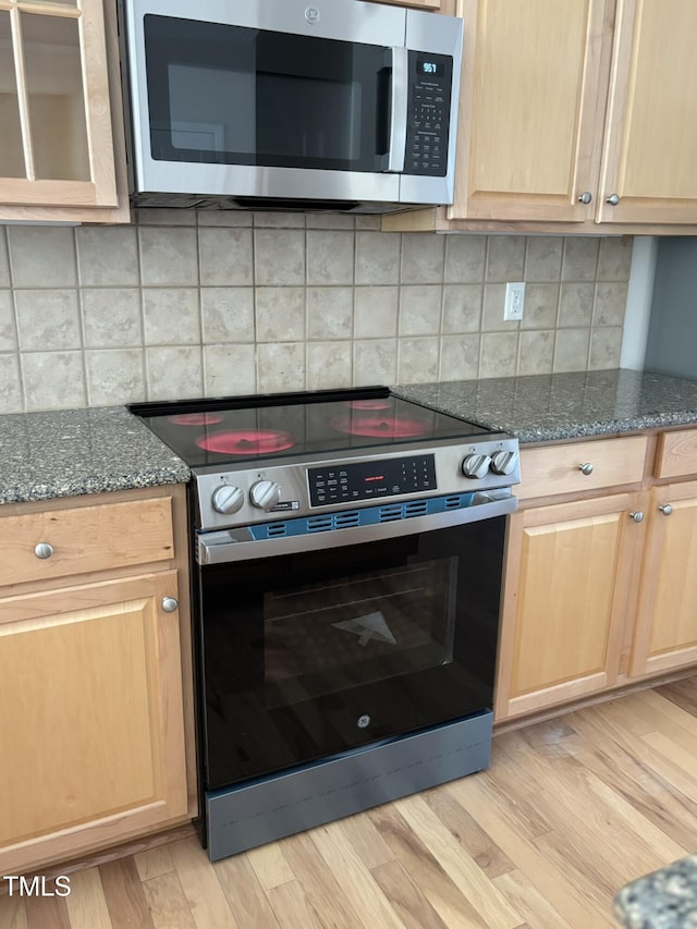 kitchen with decorative backsplash, light hardwood / wood-style flooring, dark stone counters, and appliances with stainless steel finishes