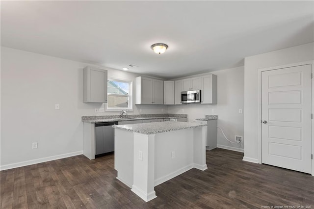 kitchen featuring gray cabinets, appliances with stainless steel finishes, light stone countertops, a kitchen island, and dark hardwood / wood-style flooring