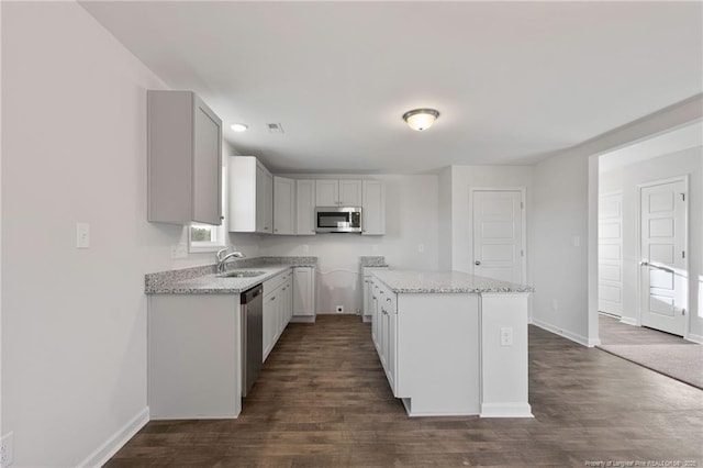 kitchen with sink, light stone counters, dark hardwood / wood-style flooring, a kitchen island, and stainless steel appliances