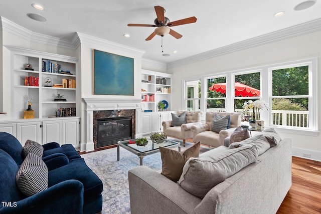 living room with ornamental molding, ceiling fan, light wood-type flooring, and a high end fireplace