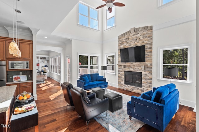 living room with a stone fireplace, ceiling fan, a high ceiling, and dark hardwood / wood-style flooring