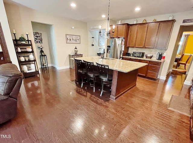 kitchen with a breakfast bar, stainless steel refrigerator with ice dispenser, wood-type flooring, and an island with sink