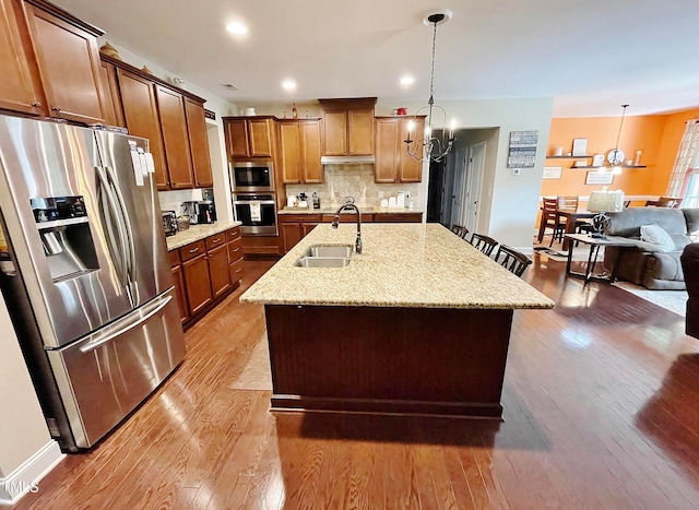 kitchen with hardwood / wood-style flooring, stainless steel appliances, hanging light fixtures, and an island with sink