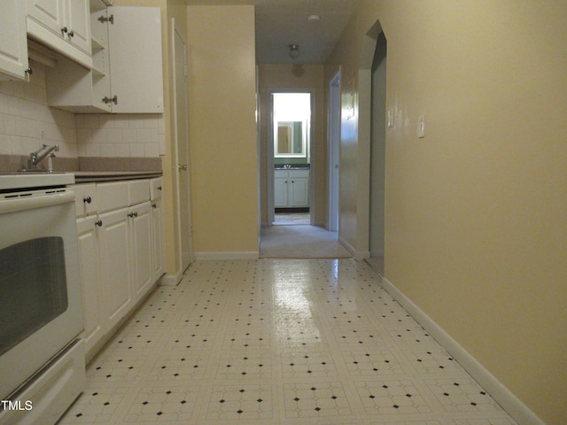 kitchen featuring white range oven, backsplash, and white cabinets