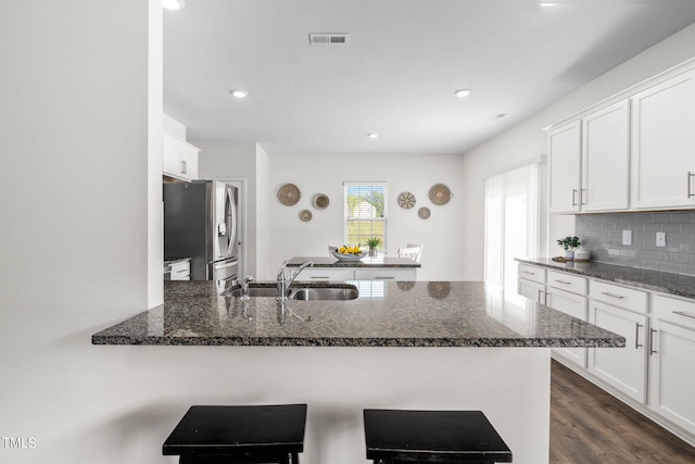 kitchen with stainless steel fridge with ice dispenser, kitchen peninsula, sink, white cabinetry, and dark stone countertops