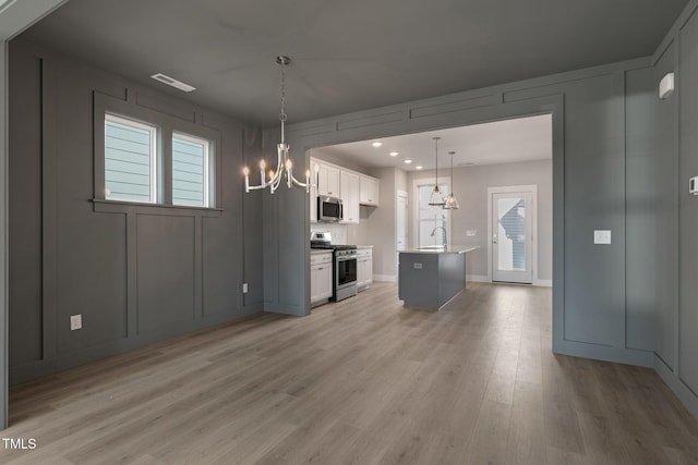 kitchen featuring an inviting chandelier, decorative light fixtures, a center island with sink, appliances with stainless steel finishes, and white cabinets