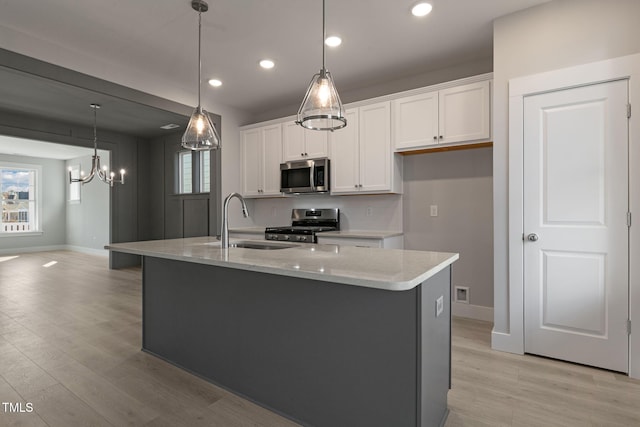 kitchen featuring sink, white cabinetry, pendant lighting, stainless steel appliances, and a kitchen island with sink