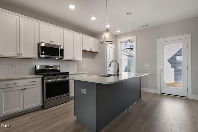 kitchen with an island with sink, sink, white cabinets, hanging light fixtures, and stainless steel appliances