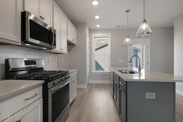 kitchen with pendant lighting, sink, appliances with stainless steel finishes, a kitchen island with sink, and white cabinetry