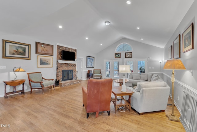 living room featuring vaulted ceiling, a brick fireplace, french doors, and light hardwood / wood-style floors