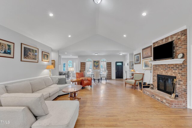 living room featuring lofted ceiling, a brick fireplace, and light hardwood / wood-style flooring