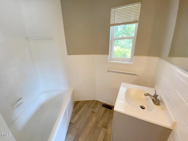 bathroom with a tub, hardwood / wood-style floors, tile walls, and vanity