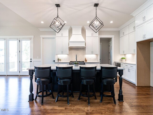 kitchen with hanging light fixtures, custom exhaust hood, white cabinets, and dark hardwood / wood-style flooring