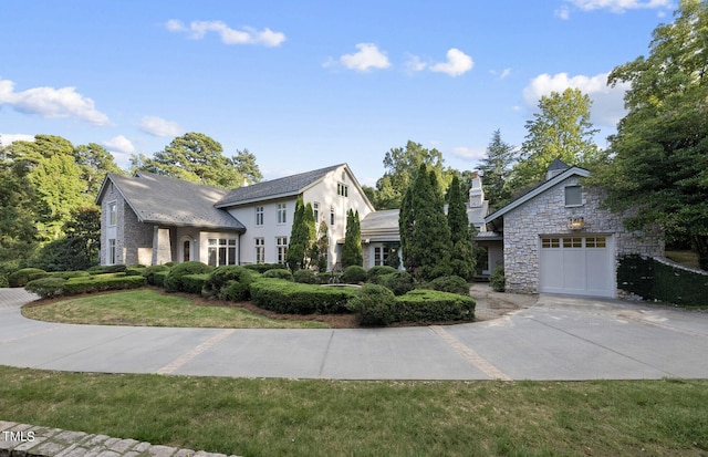 view of front of home featuring stucco siding, a front lawn, stone siding, a garage, and a chimney