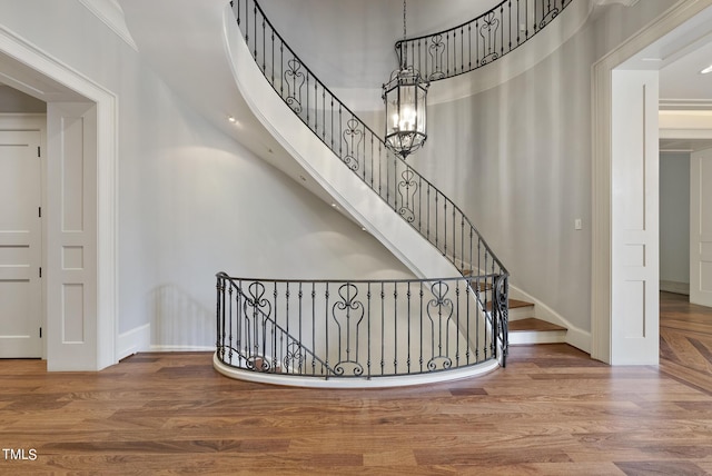 stairs featuring a chandelier, baseboards, wood finished floors, and a towering ceiling