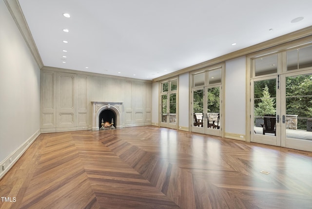 unfurnished living room with a wealth of natural light, french doors, a lit fireplace, and crown molding