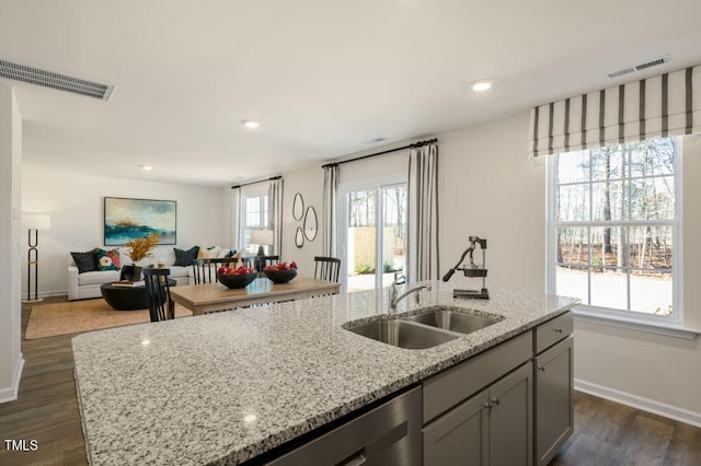 kitchen featuring a kitchen island with sink, light stone counters, sink, dark wood-type flooring, and gray cabinetry