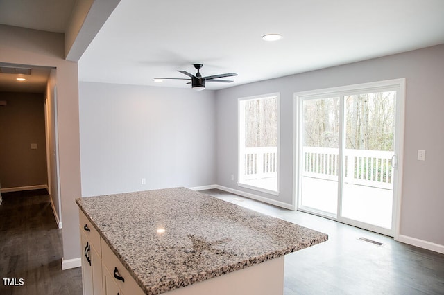 kitchen featuring light stone counters, white cabinetry, dark wood-type flooring, ceiling fan, and a kitchen island