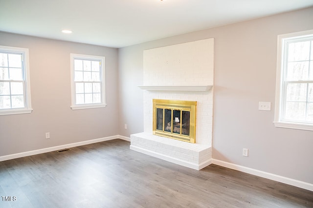 unfurnished living room with a brick fireplace, hardwood / wood-style floors, and a wealth of natural light