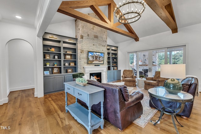 living room featuring built in shelves, a stone fireplace, beam ceiling, light hardwood / wood-style floors, and a chandelier